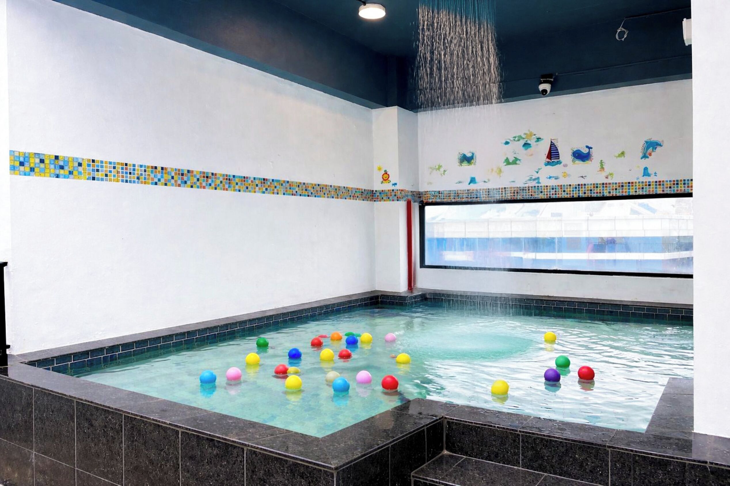 A swimming pool with colorful balls and a water feature.