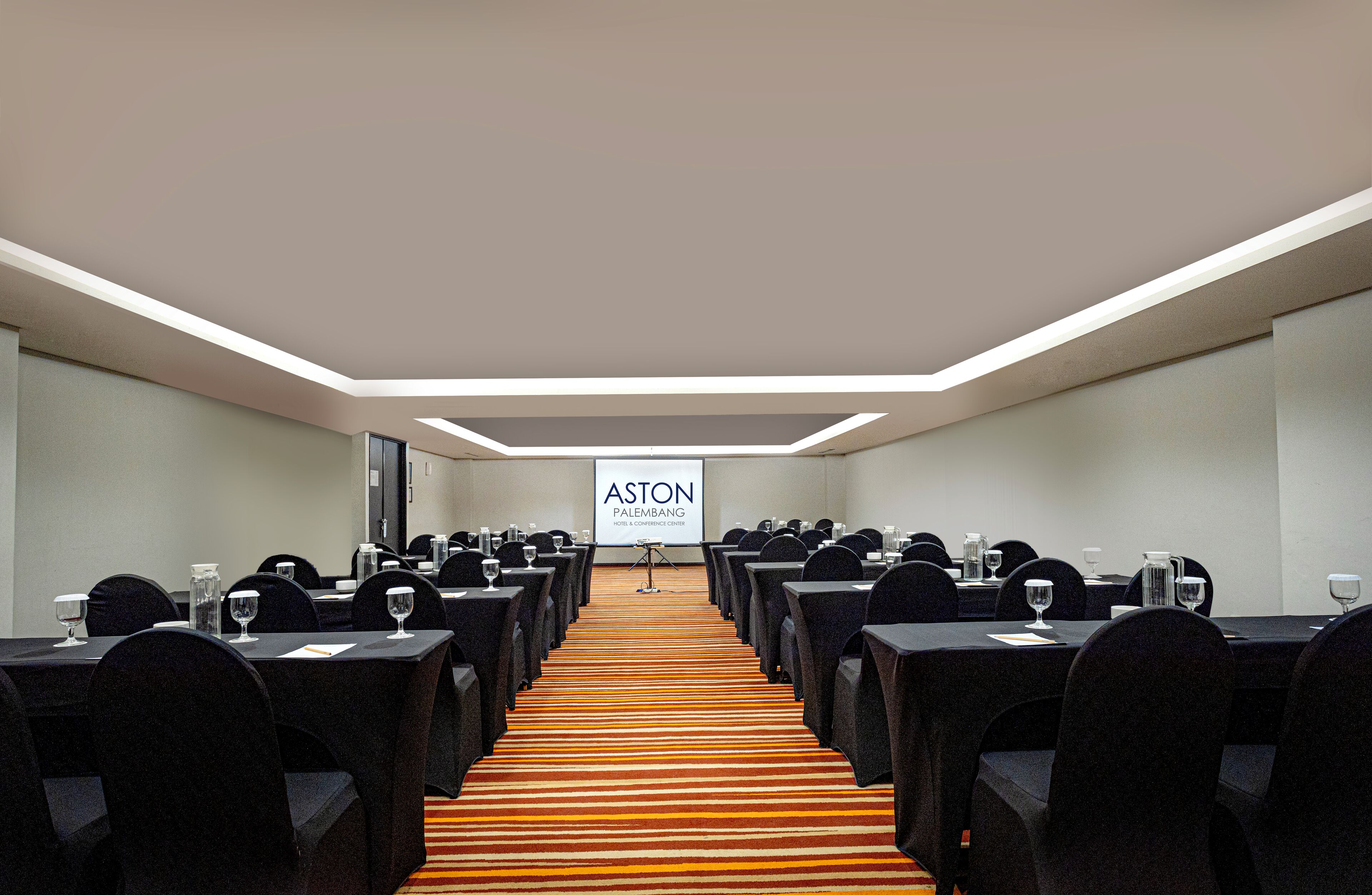 A conference room with tables and chairs arranged for a meeting, a podium with a screen, and a carpeted floor.