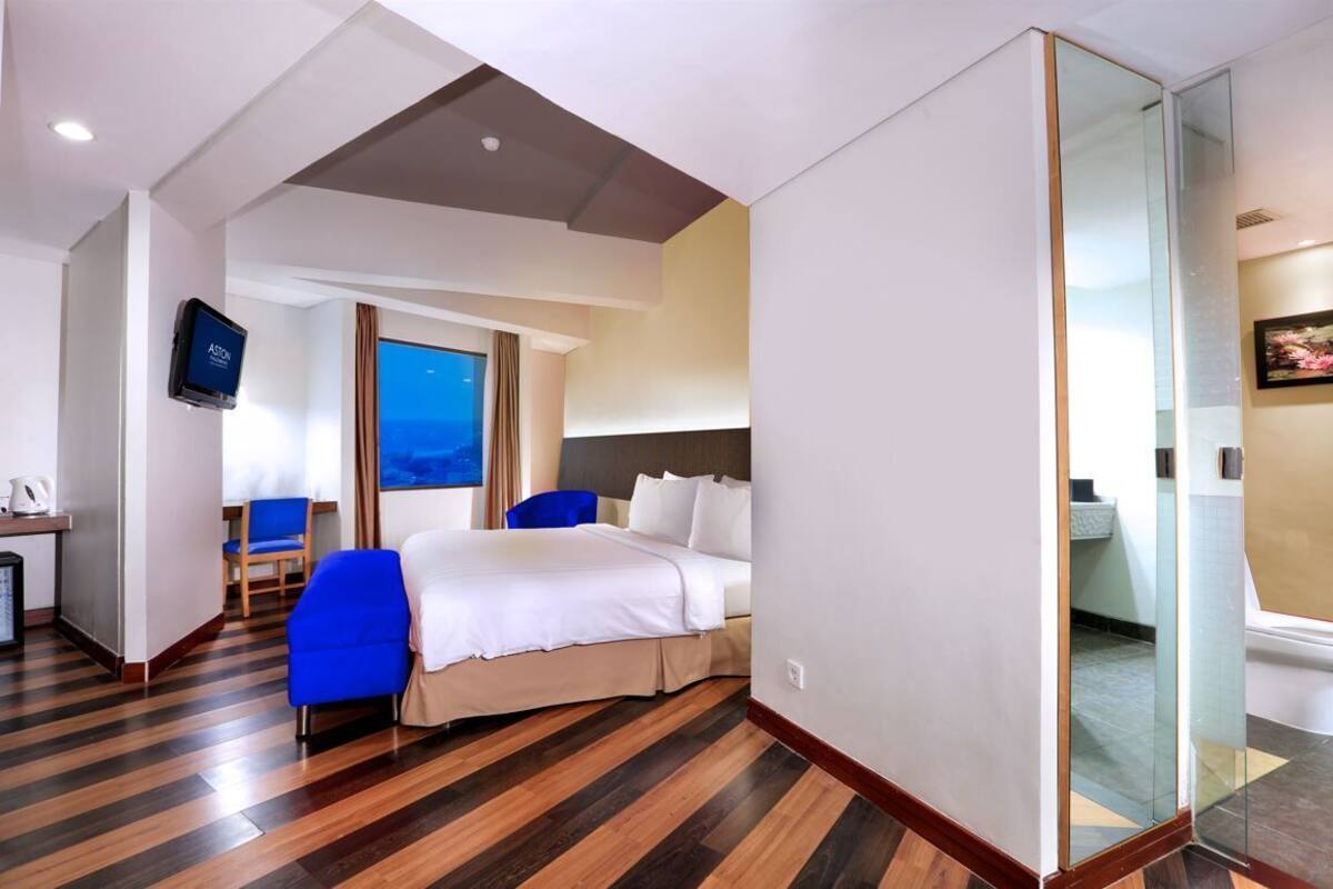 A hotel room with a bed, a desk with a computer, a chair, and a television.