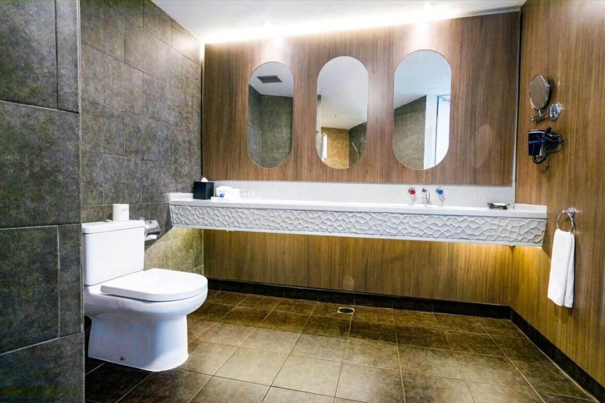A modern bathroom with a white toilet, a wooden vanity with a mirror, and a towel hanging on the wall.
