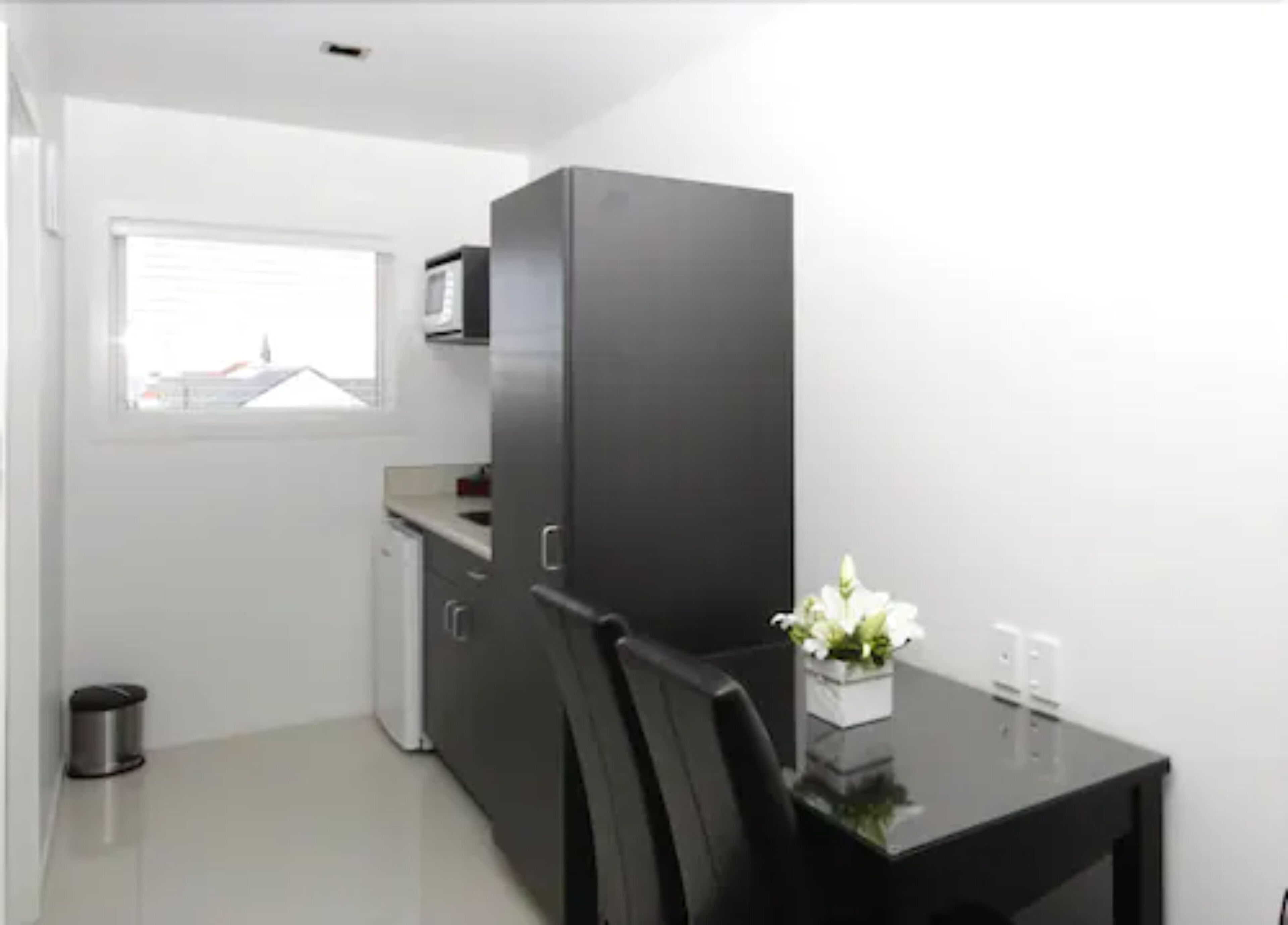 A compact kitchen with a microwave, a small refrigerator, and a dining table with chairs.