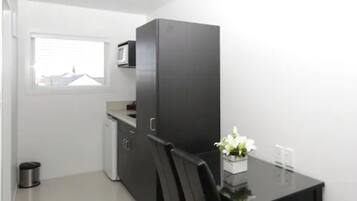 A compact kitchen with a microwave, a small refrigerator, and a dining table with chairs.