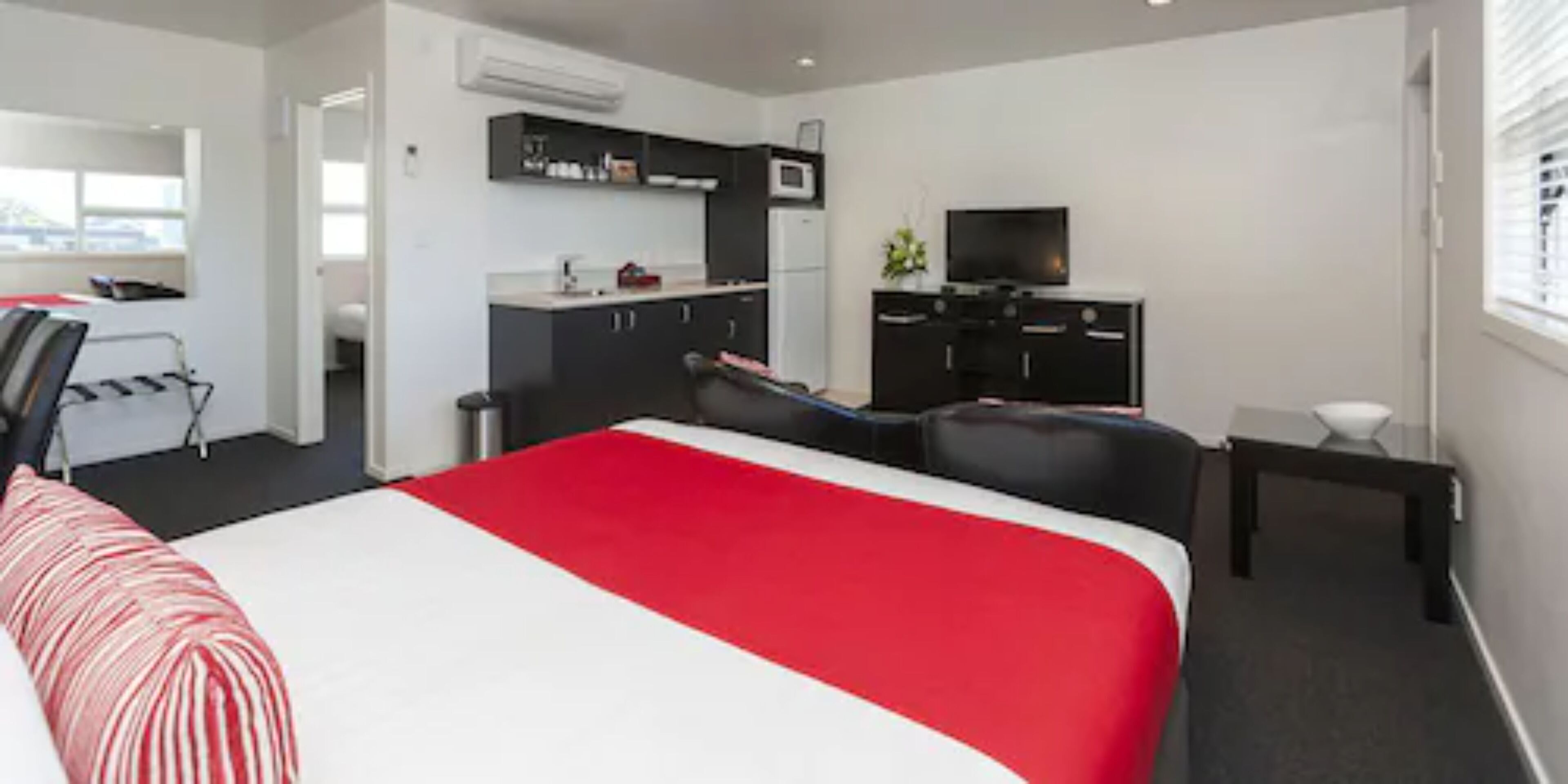 A hotel room with a bed, a desk, a chair, a TV, and a kitchenette.