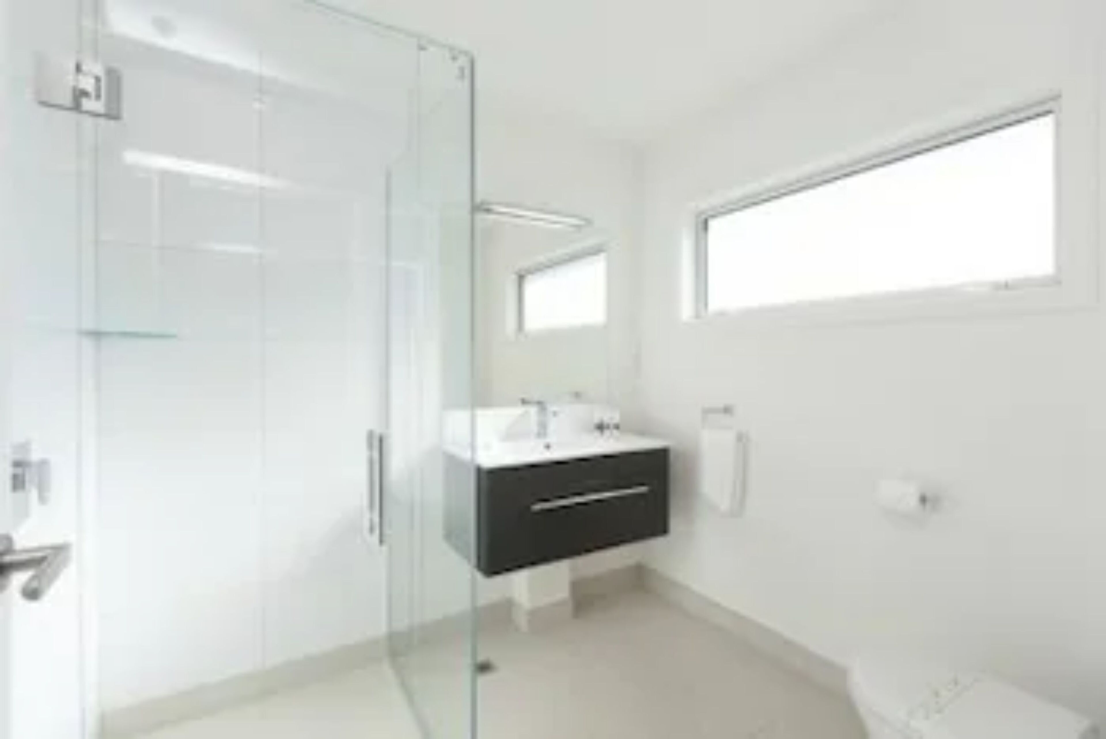 A modern bathroom with a glass shower enclosure, a white sink vanity, and a large window providing natural light.