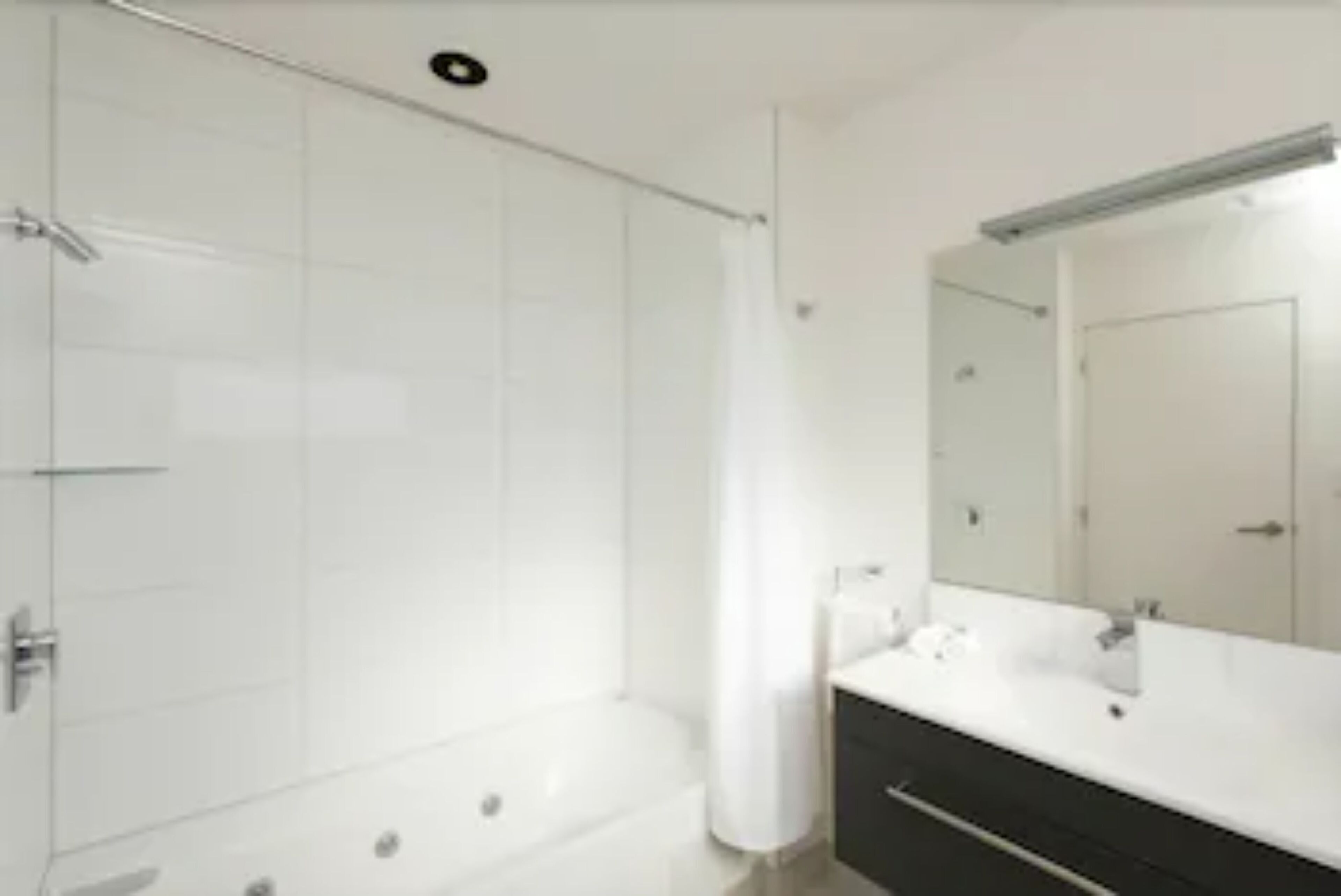 A modern bathroom with a bathtub, a large mirror, and a white vanity.