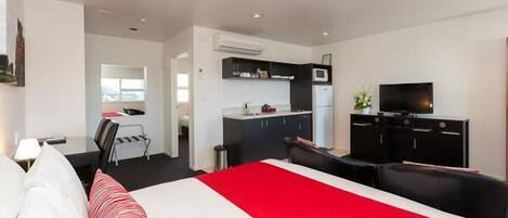 Una habitación de hotel con cama, escritorio, silla, televisor y kitchenette.