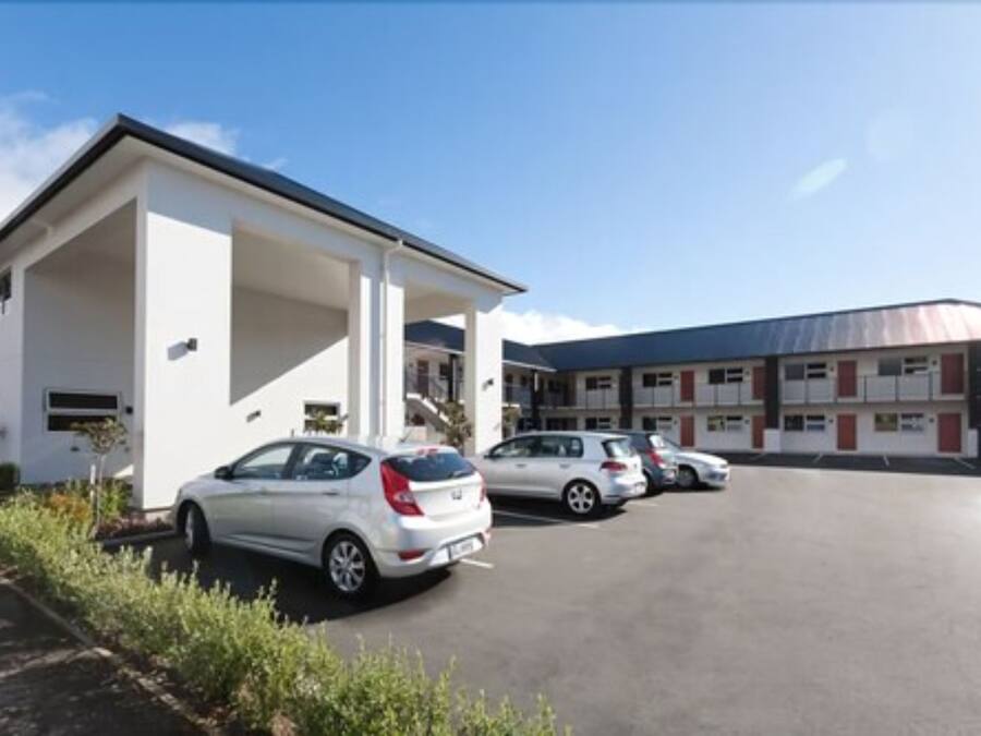 A building with a covered parking area and several cars parked in front.