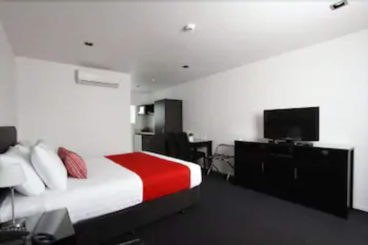 Una habitación de hotel moderna con una cama grande, un escritorio, un televisor y un armario.