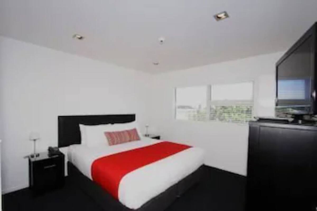 Una habitación de hotel con cama, mesita de noche, televisor y ventana con vista a la ciudad.