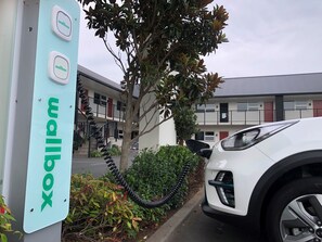 A wallbox for electric vehicles, a white car parked nearby, and a building with balconies and windows. - The Dawson Motel (New Plymouth)