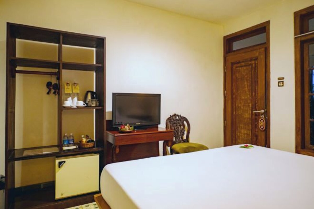 A hotel room with a bed, a television on a wooden stand, a wardrobe, and a door.