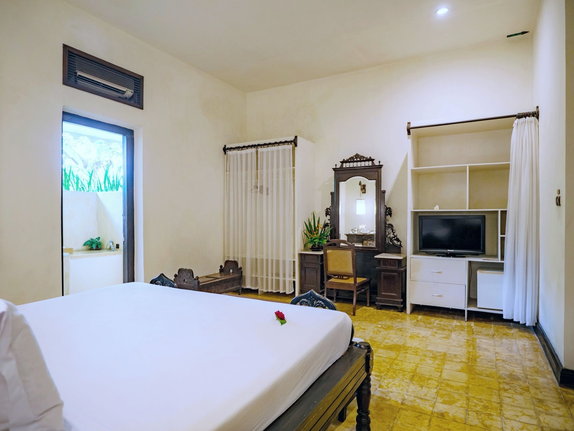 A hotel room with a bed, a desk with a mirror, a television, and a window with curtains.