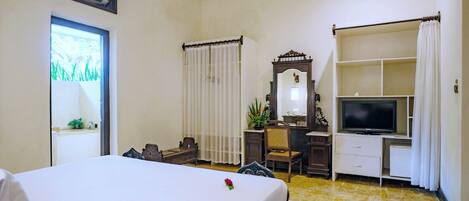 A hotel room with a bed, a desk with a mirror, a television, and a window with curtains.