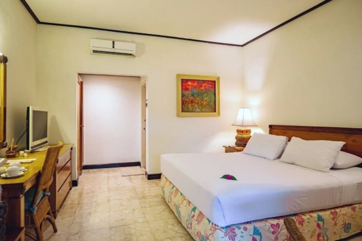 A hotel room with a bed, a desk with a computer, a lamp, and a painting on the wall.