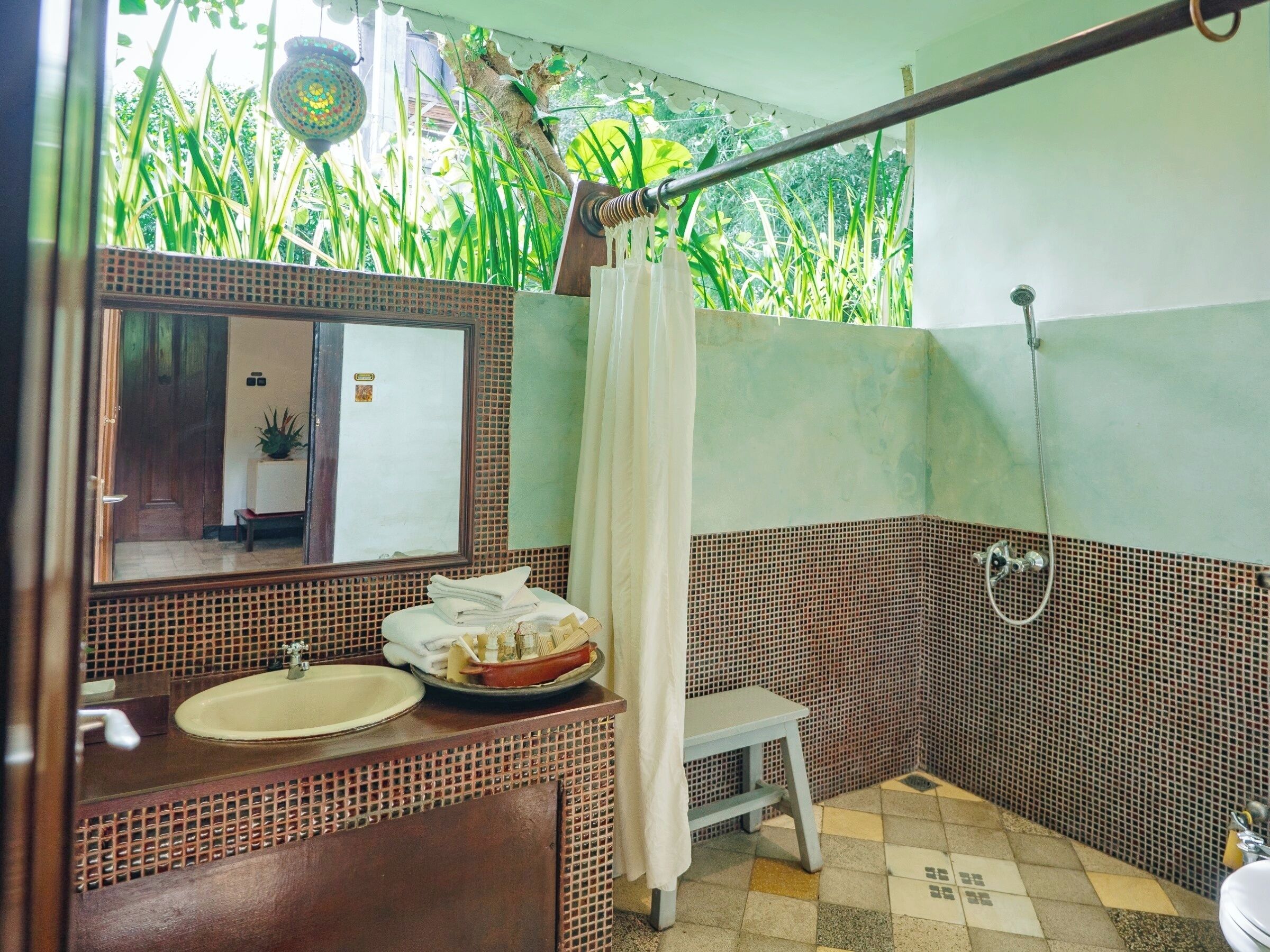 A bathroom with a sink, mirror, shower, and a small stool.