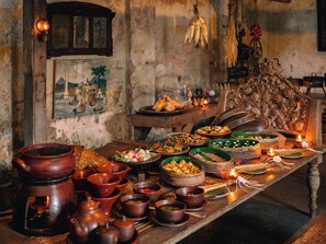 A traditional wooden table with various dishes and pottery, set in a rustic room with stone walls and a hanging light fixture.