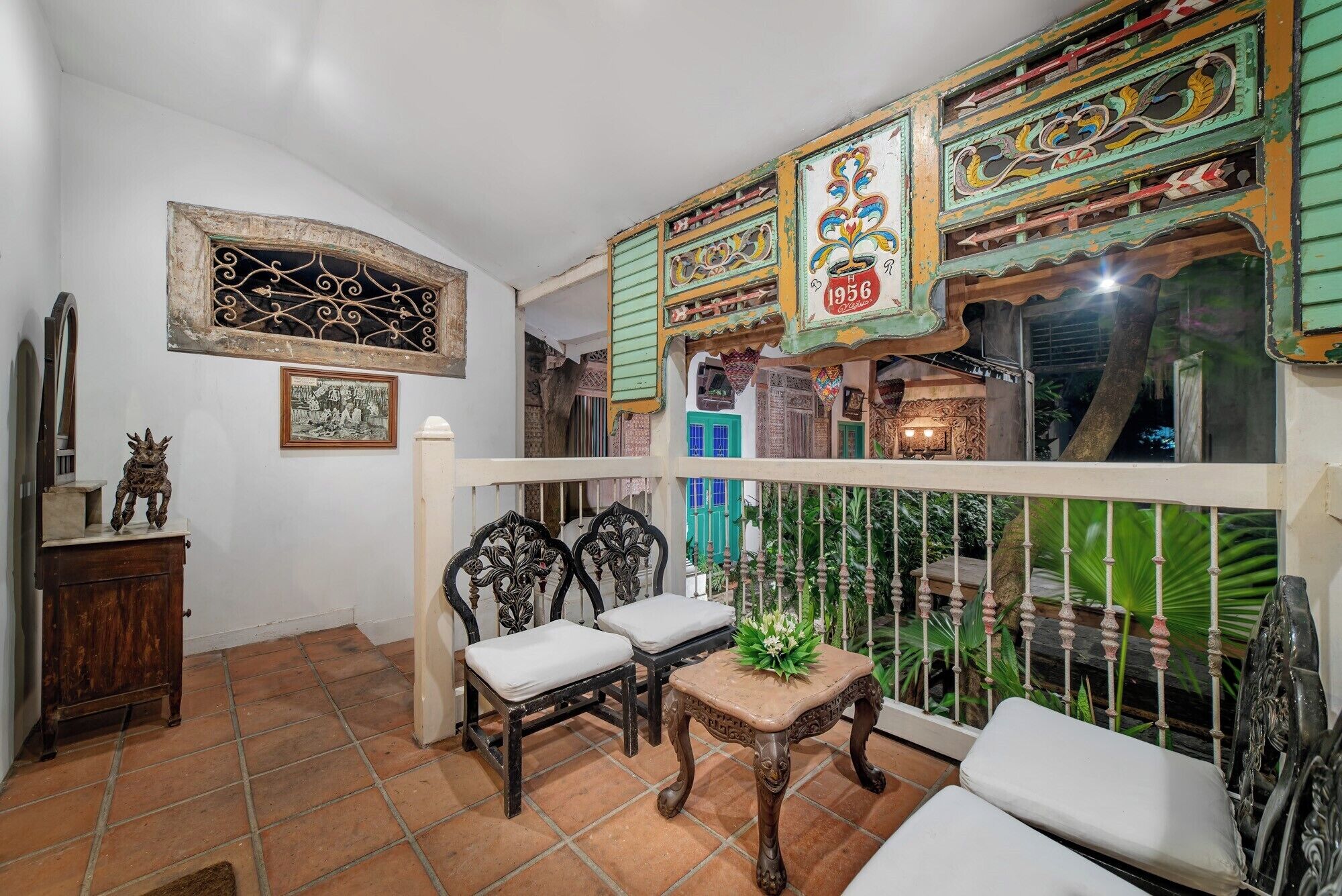A traditional room with a balcony, a wooden chair, a small table with a cushion, and a decorative wall with a year plaque.