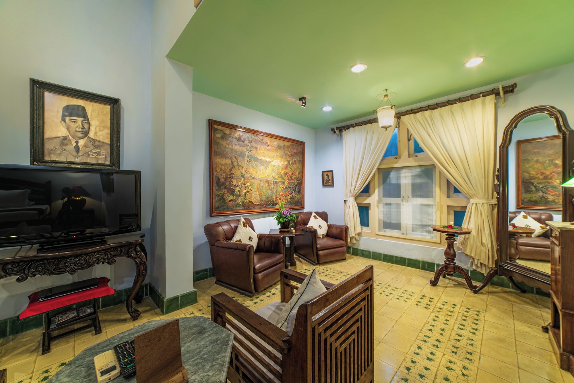 A living room with a television, leather sofas, a large painting, and a window with curtains.