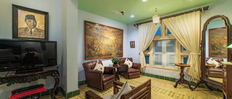 A living room with a television, leather sofas, a large painting, and a window with curtains.