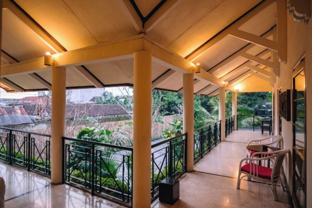 A covered outdoor area with a balcony, columns, and a chair.