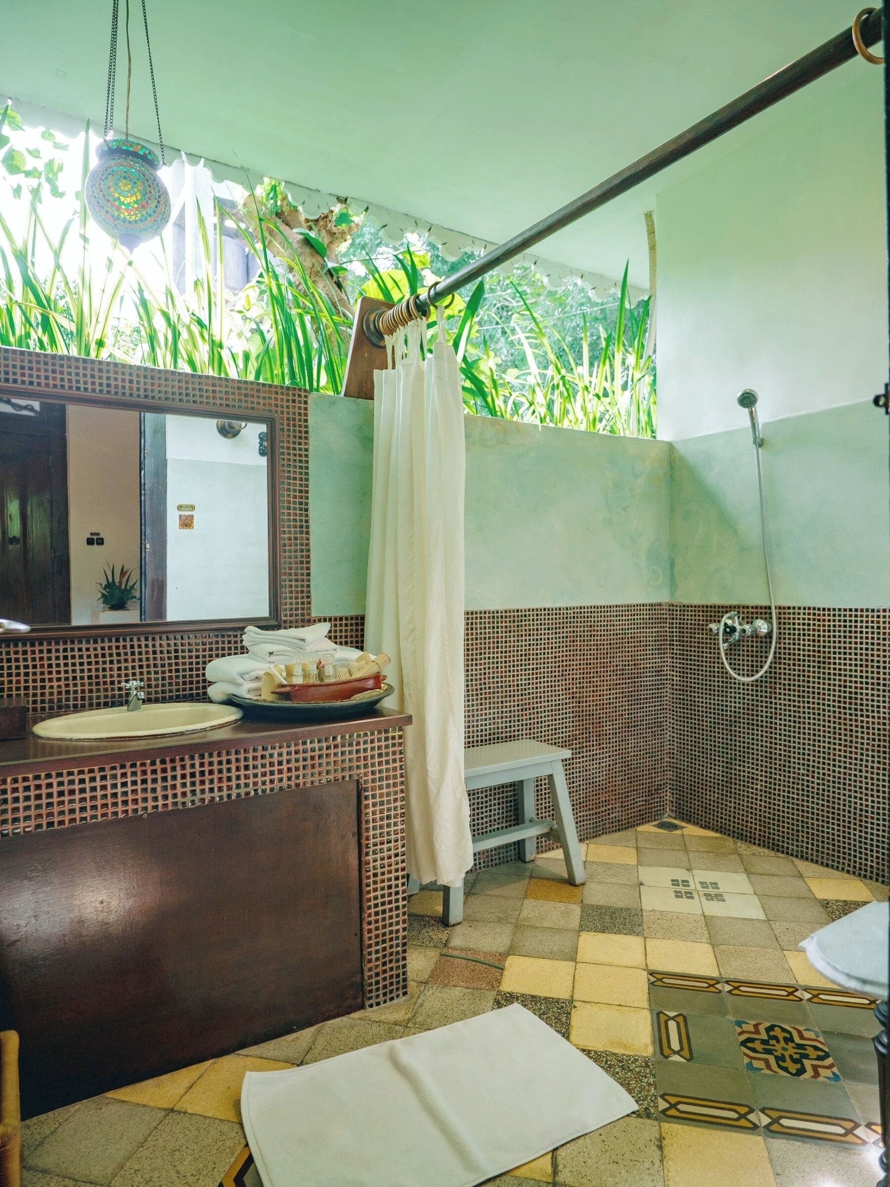 A bathroom with a sink, mirror, shower, and a small stool.