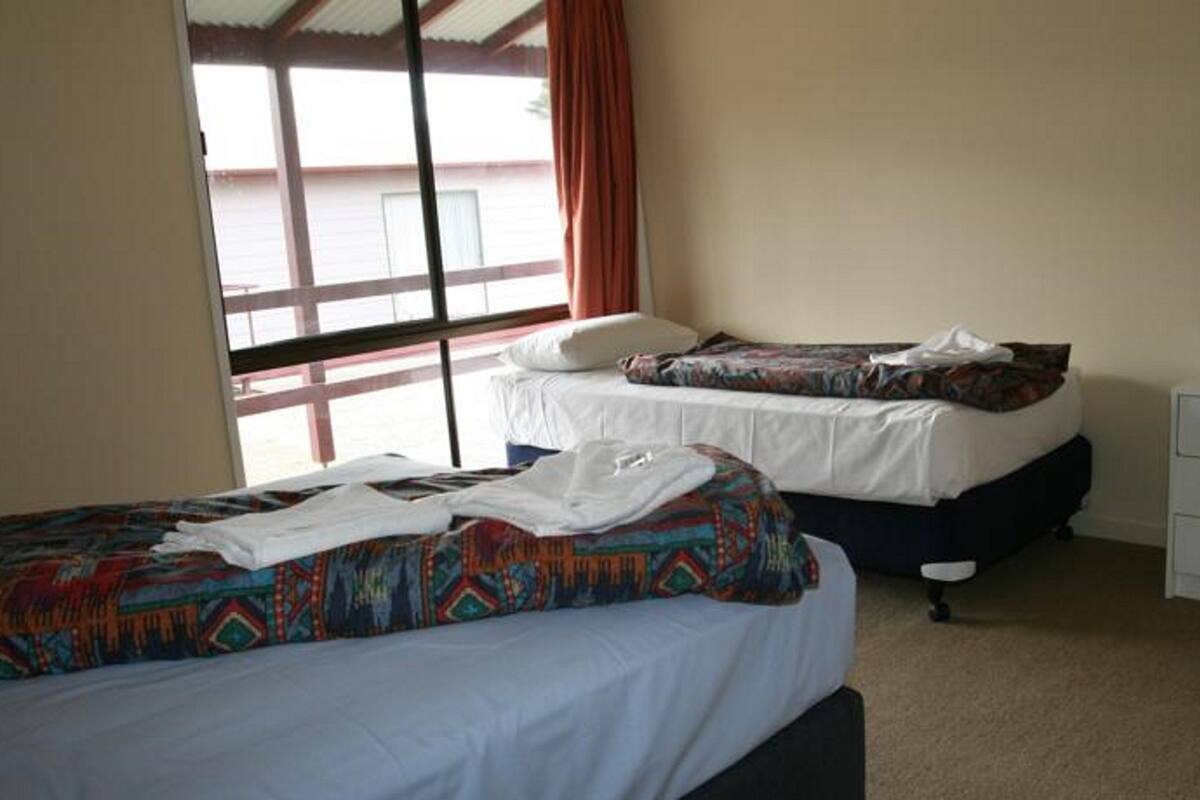 A hotel room with two beds, a window with curtains, a white dresser with drawers, and a carpeted floor.