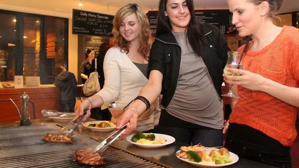 A group of people at a restaurant with a menu board in the background. - The Station (Jindabyne)