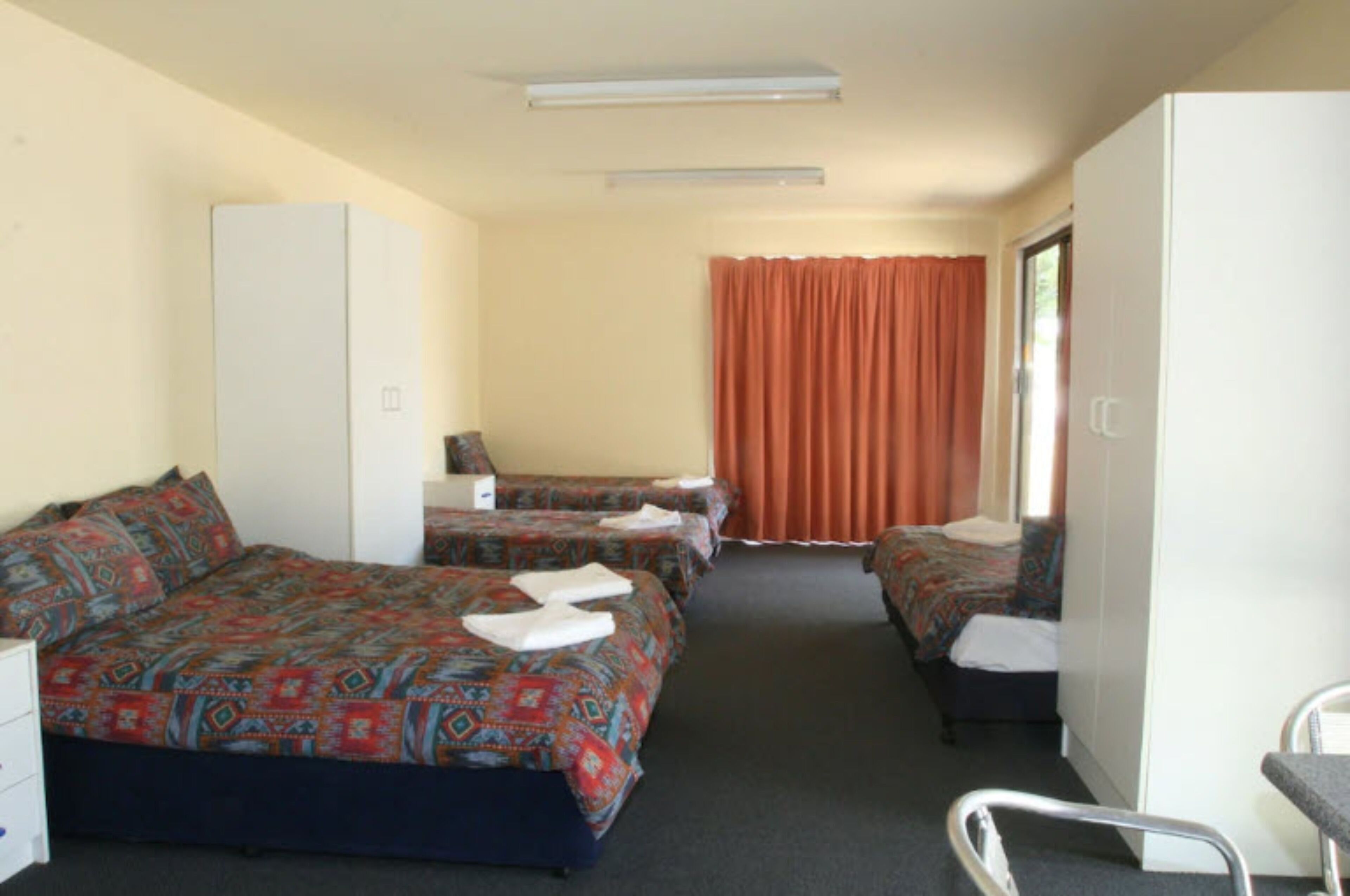 A hotel room with two beds, a desk, a chair, and a wardrobe.