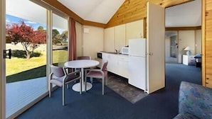 A compact room with a dining table and chairs, a kitchenette, and a large sliding glass door leading to an outdoor area. - The Station (Jindabyne)