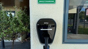 Una estación de carga para vehículos eléctricos con enchufe BMW, un letrero que indica que es solo para huéspedes y una planta en maceta cerca.