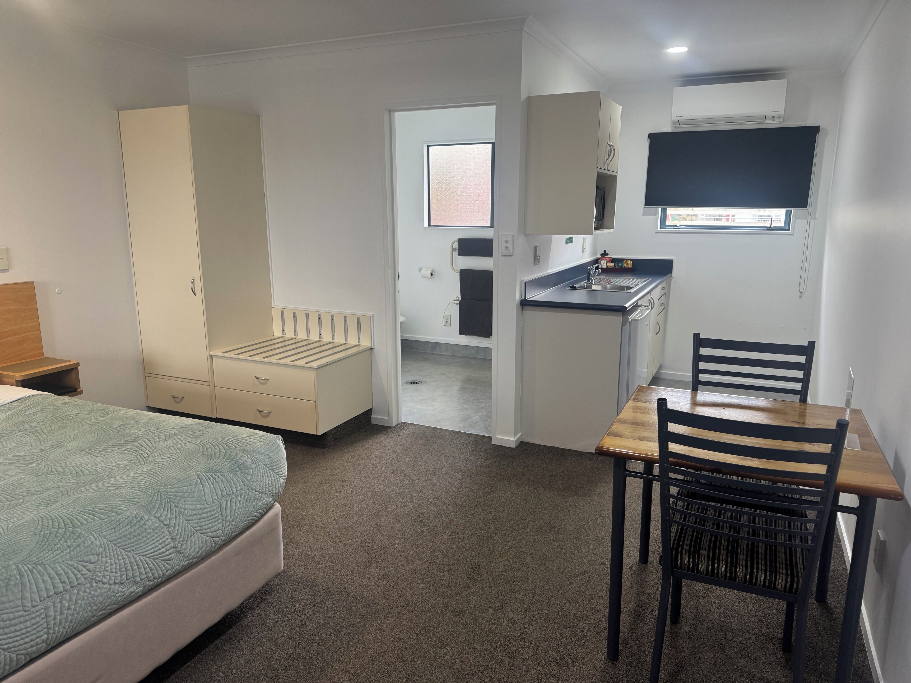 A compact room with a bed, a desk, a chair, a wardrobe, and a kitchenette.