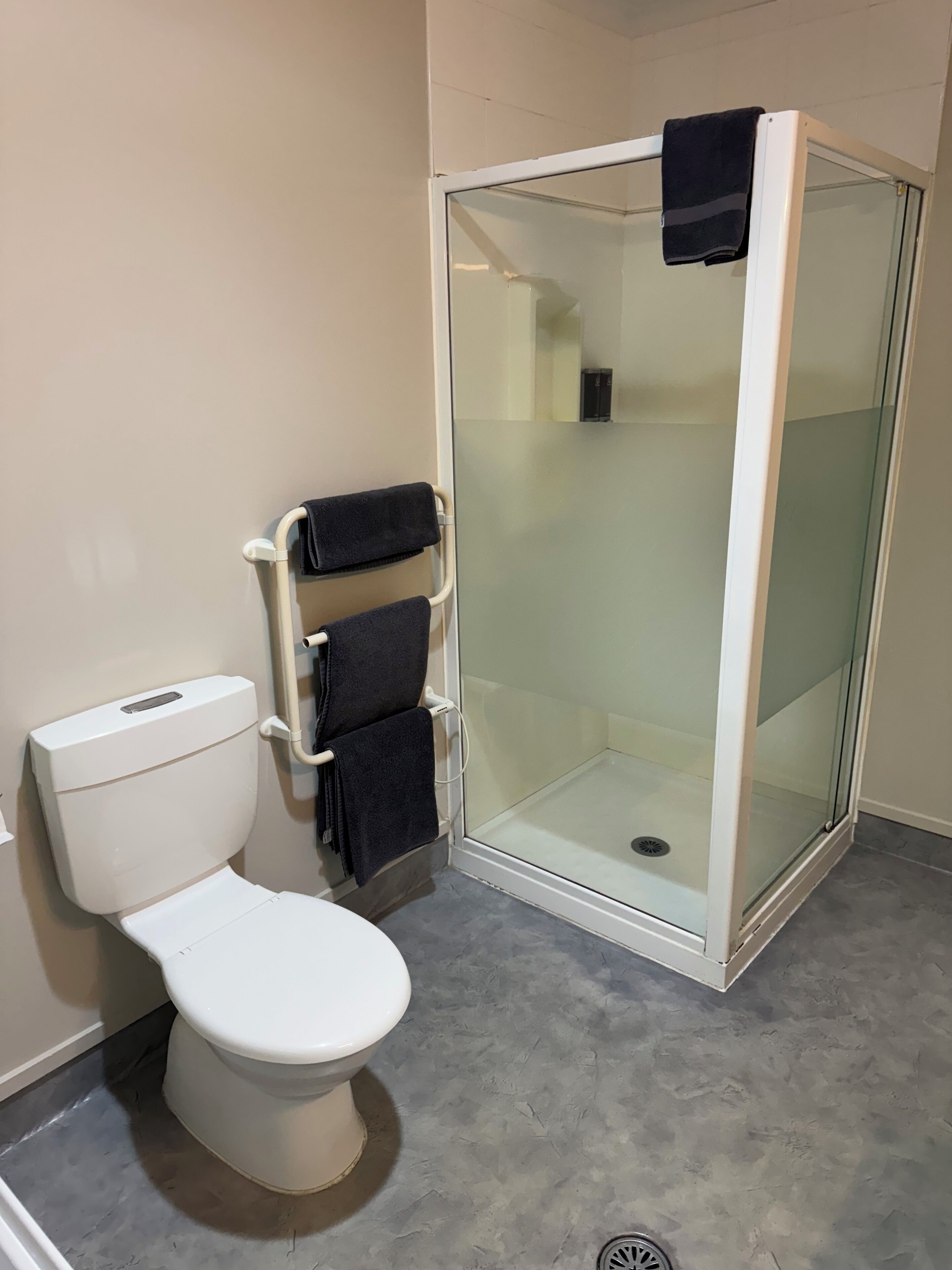 Un baño con inodoro blanco, ducha con cerramiento de vidrio y un perchero con dos toallas.
