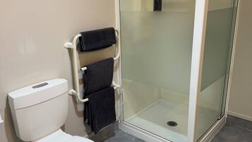 Un baño con inodoro blanco, ducha con cerramiento de vidrio y un perchero con dos toallas.