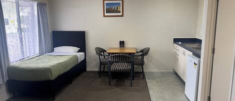 Una habitación compacta con cama, una pequeña mesa de comedor con sillas, una kitchenette y un cuadro en la pared.