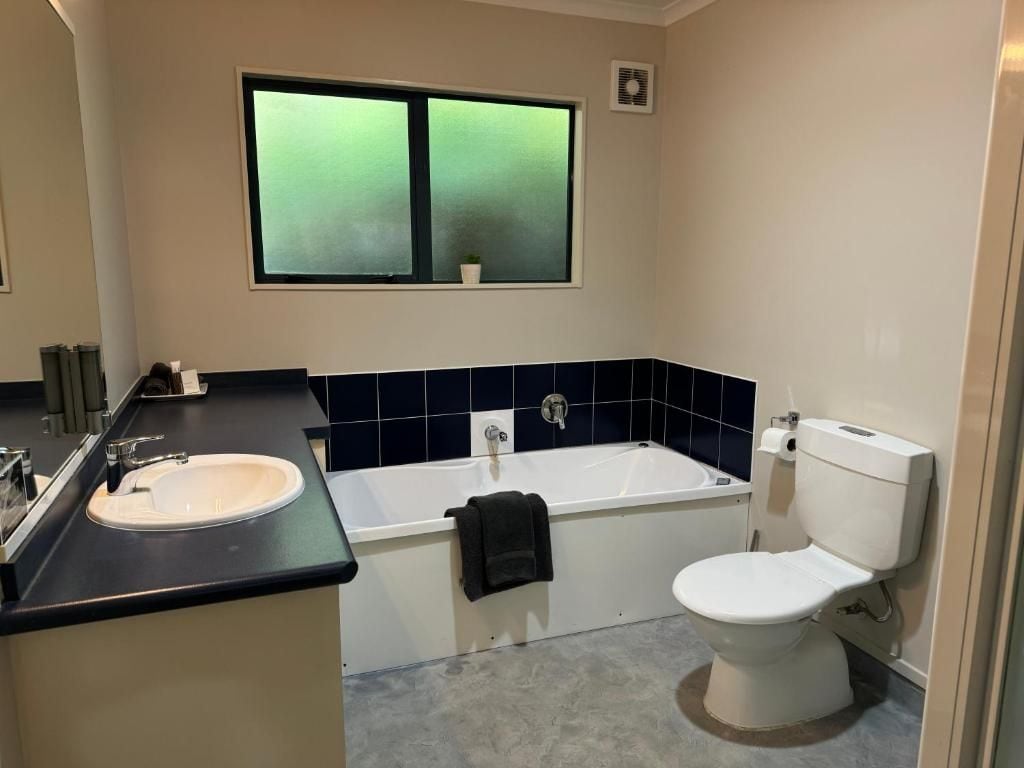 Un baño con bañera, inodoro, lavamanos y ventana con vistas.