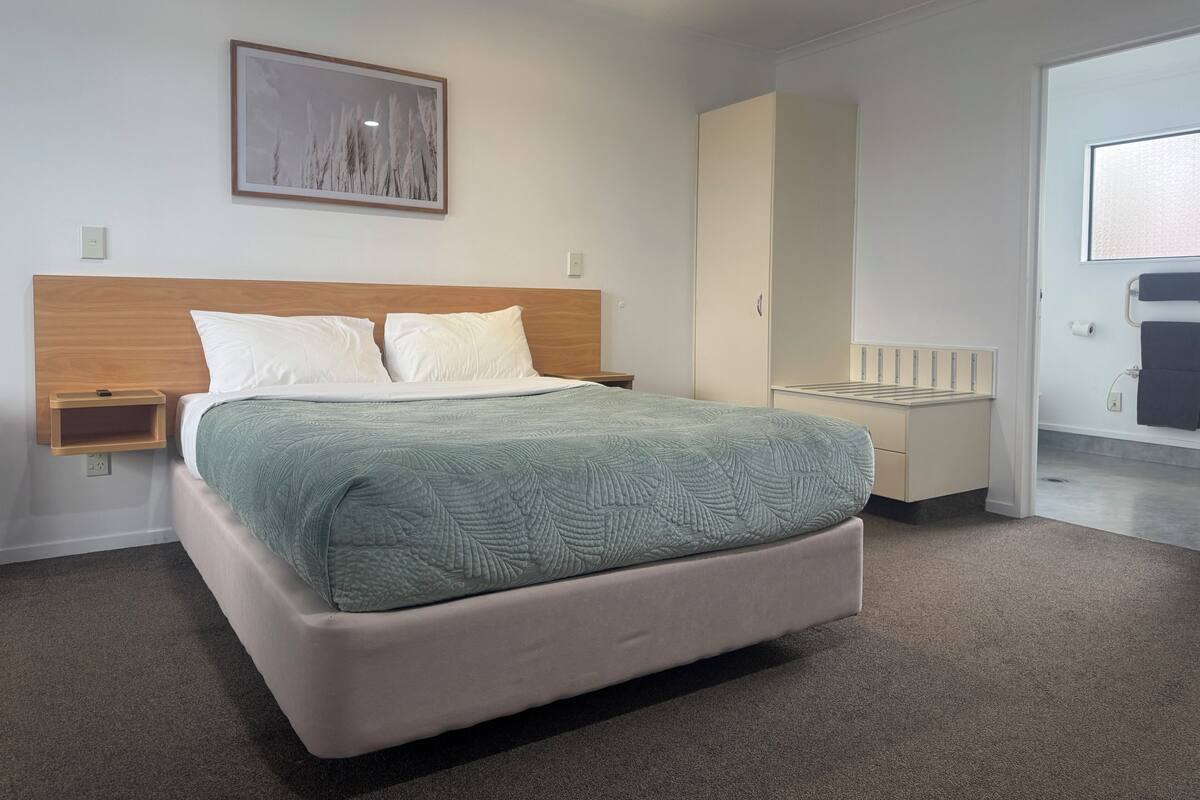 A modern bedroom with a bed, a nightstand, a wardrobe, and a bathroom visible through an open door.
