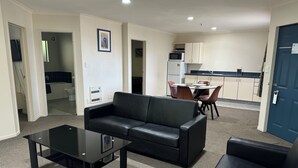 Una sala de estar con un sofá de cuero negro, una mesa de centro de vidrio y un comedor con mesa blanca y sillas marrones.