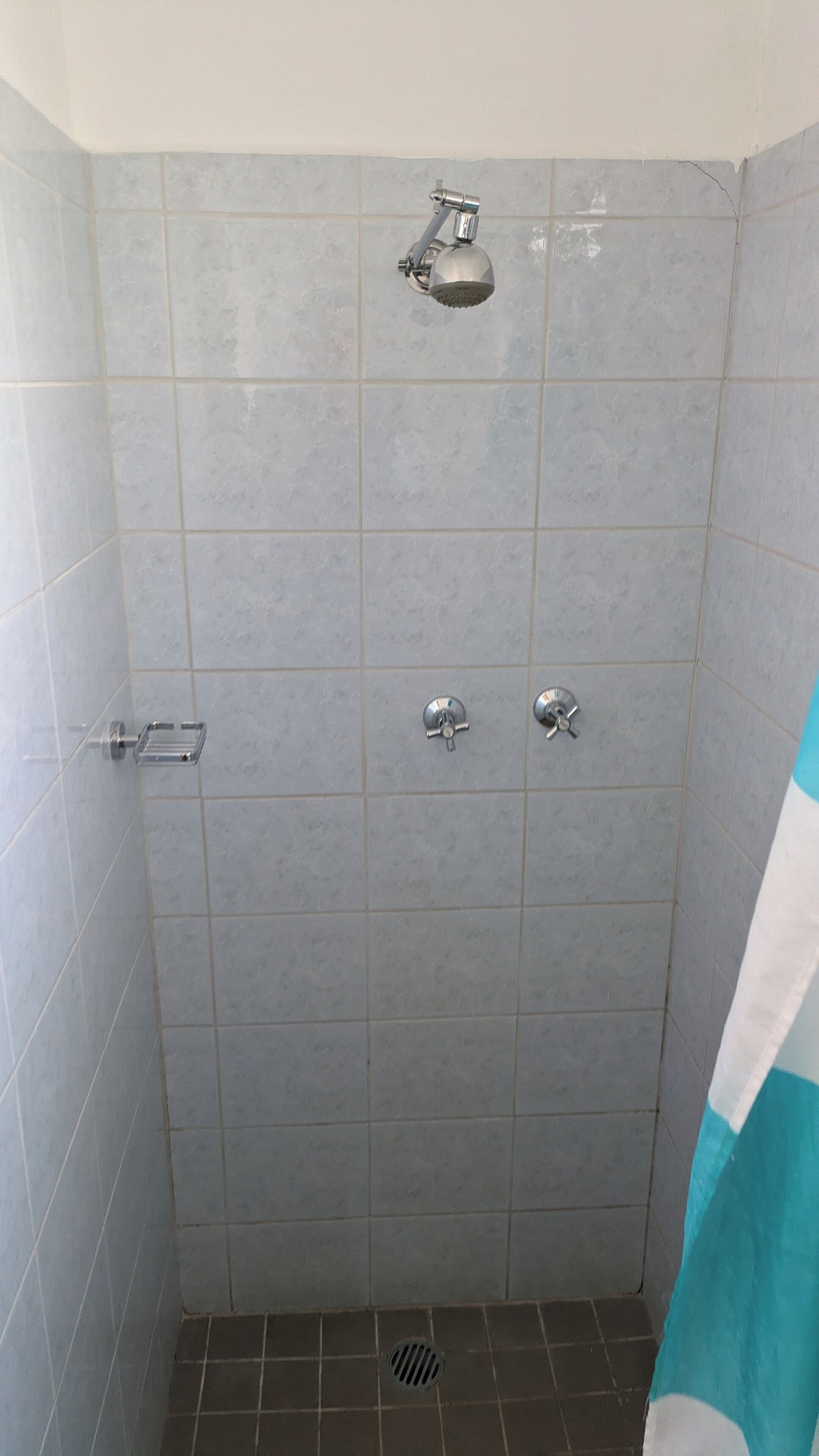 A shower with a handheld showerhead and two wall-mounted faucets.
