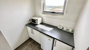 A compact kitchen with a microwave, a small refrigerator, and a window with a view of the outside. - Top of the Town Motel Narooma (Narooma)
