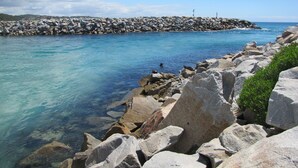 A rocky shoreline with clear blue water and a distant rocky breakwater. - Top of the Town Motel Narooma (Narooma)