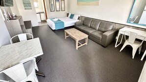A hotel room with a bed, a sofa, a desk, and a chair. There is a painting on the wall and a mirror above the desk. - Top of the Town Motel Narooma (Narooma)