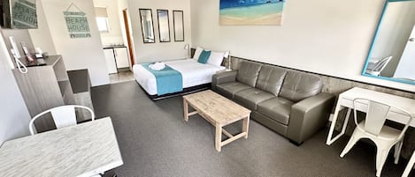 Quarto de hotel com uma cama, um sofá, uma escrivaninha e uma cadeira. Há um quadro na parede e um espelho sobre a escrivaninha.