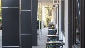 A row of outdoor tables and chairs along a covered walkway, with large black pillars and a building with large windows on the right. - Top of the Town Motel Narooma (Narooma)