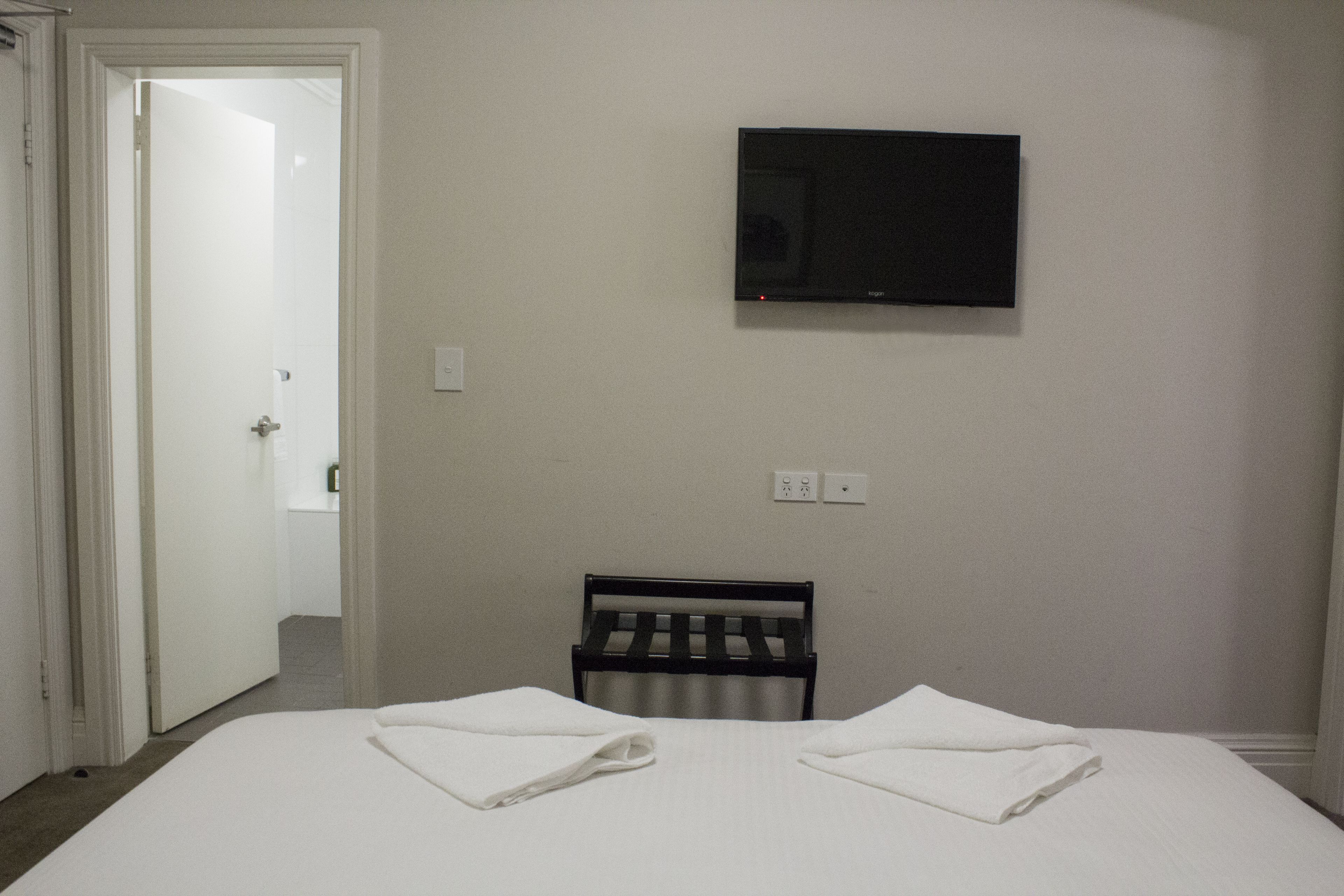 Una habitación de hotel con una cama, un televisor instalado en la pared y una silla.