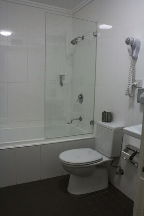 A bathroom with a glass-enclosed shower, a toilet, and a hairdryer mounted on the wall. - Wallacia Hotel (Wallacia)