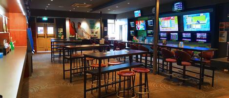 A restaurant with multiple tables and chairs, a bar area, and several screens displaying sports events.