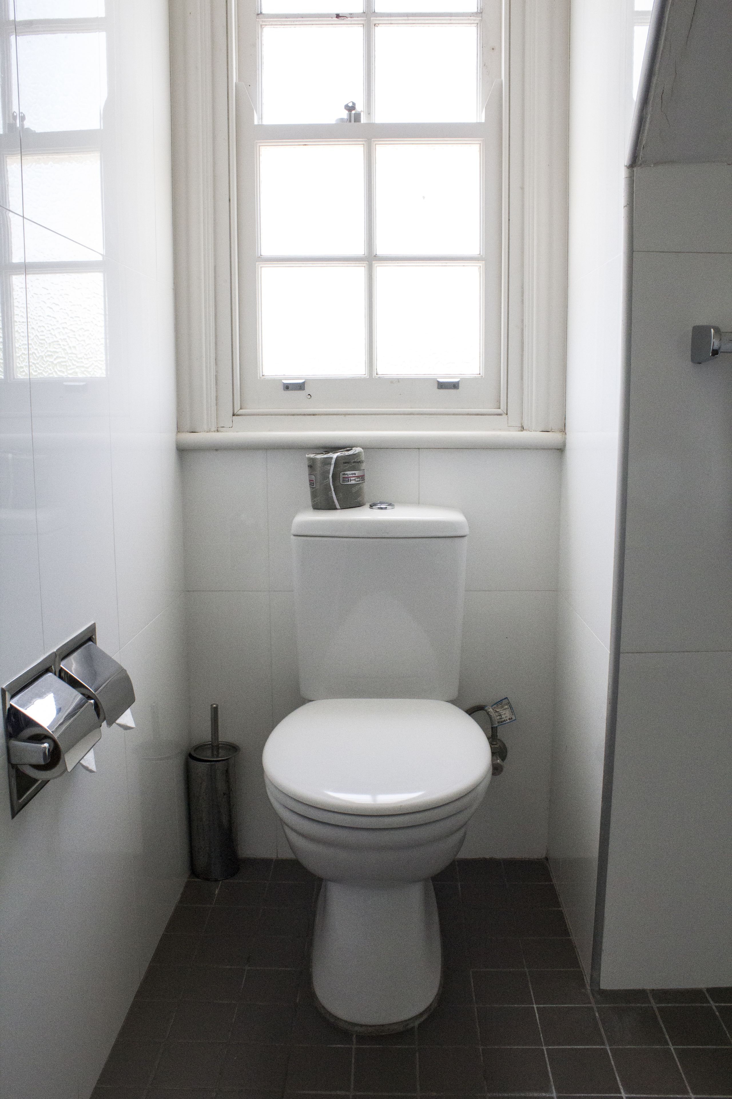 A small, clean bathroom with a toilet, a window, and a trash can.