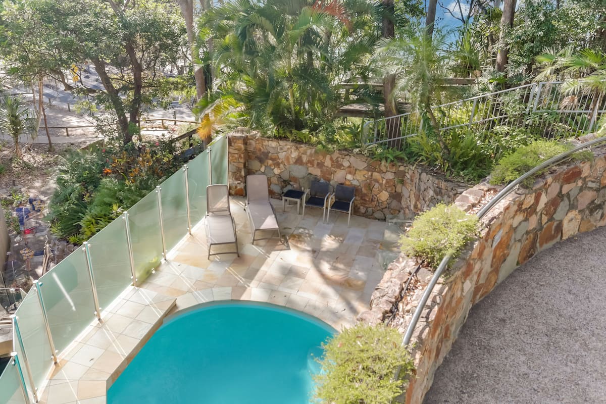 A pool area with a stone wall, glass railing, and lounge chairs.