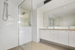 A modern bathroom with a glass shower enclosure, a large mirror, and white cabinetry. - Little Cove Court (Noosa Heads)