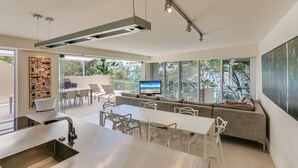 A modern kitchen with a large island, dining area, and a living space with a TV. - Little Cove Court (Noosa Heads)